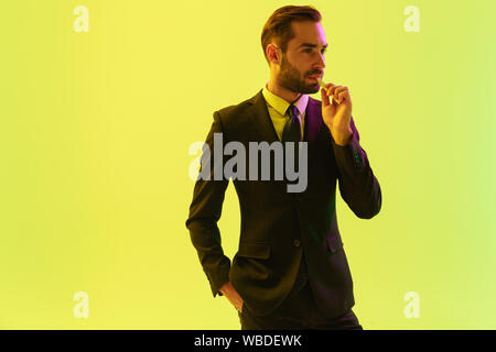Image of a serious young business man posing isolated over light green background wall with led neon lights smoking electronic cigarette. Stock Photo