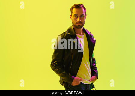 Image of young stylish man posing isolated over light green background wall with led neon lights dressed in leather jacket. Stock Photo