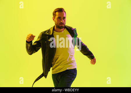 Attractive young man wearing leather jacket jumping isolated over yellow background Stock Photo