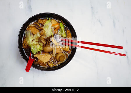 A vegan mushroom and tofu based Asian noodles clear soup, served in a black bowl with red chopsticks at a restaurant in Singapore. Stock Photo