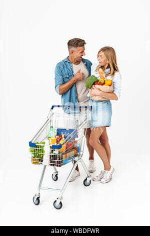 Photo of caucasian couple woman and man holding food products in supermarket and carrying shopping cart isolated over white background Stock Photo