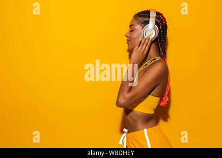 Image of pretty african american woman wearing afro braids listening to music with headphones isolated over yellow background Stock Photo
