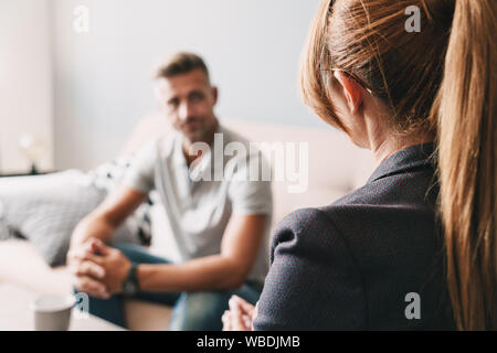 Photo of caucasian focused man having conversation with psychologist on therapy session in room Stock Photo