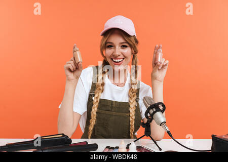 Image of adorable girl recording blog broadcast with microphone about new cosmetic products isolated over orange wall in studio Stock Photo