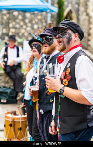 Sandwich folk and Ale Festival event, UK. Traditional English folk dancers, Dead Horse morris side, with blackened faces, standing in street, singing. Stock Photo