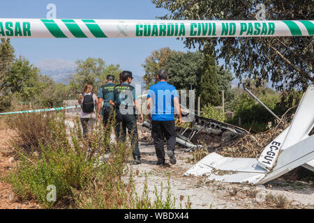 Inca, Spain. 26th Aug, 2019. A crash site is closed with a barrier tape of the 'Guarda Civil', members of the police unit 'Guardia Civil' stand with two other persons behind a part of the airplane wreckage. On 25.08.2019, an ultralight aircraft and a helicopter collided over the Spanish holiday island of Mallorca - with fatal consequences. Among the seven fatalities are also four Germans, as the Foreign Office confirmed on Monday. They were a couple from Munich as well as their eleven-year-old son and nine-year-old daughter. Credit: Tomeu Coll/dpa/Alamy Live News Stock Photo