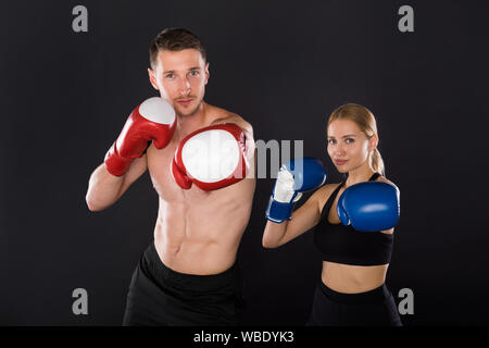 Couple exercising punching. Young woman and man in boxing gloves on the black background. Stock Photo
