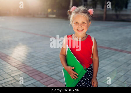 Child ready for primary school. Happy pupil girl wearing backpack and holding file. Education concept. Back to school Stock Photo