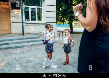 Happy mother waving to her daughters before classes outdoors primary school seeing them off. Family saying goodbye. First day of school Stock Photo