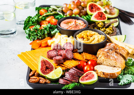 Meat and Cheese appetizer Platter. Sausage, cheese, hummus, vegetables, fruits and bread on a black tray, white background. Stock Photo