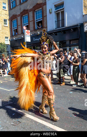 26 August 2019 - Samba dancer with orange feather wings walking in the parade, Notting Hill Carnival on a hot Bank Holiday Monday, London, UK