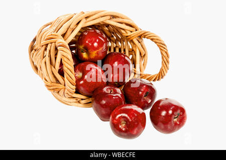 Horizontal shot of a small woven basket with handles on its side with shiny red apples spilling out on a white background.  Copy space. Stock Photo