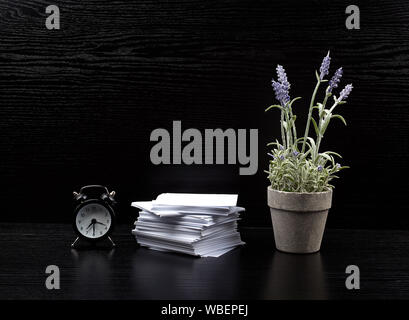 stack of white square note papers, a ceramic pot of lavender and an alarm clock on a black office desk, Scandinavian style Stock Photo