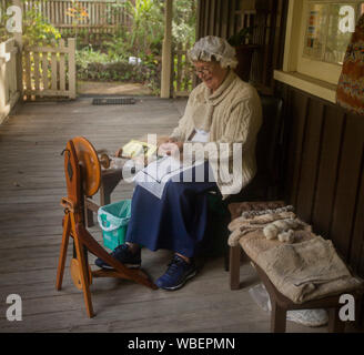 Woman in period dress sitting on cottage verandah spinning wool with spinning wheel in NSW Australia Stock Photo