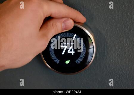 Hand adjusting temperature on smart thermostat to save energy and money. Green tech! Stock Photo