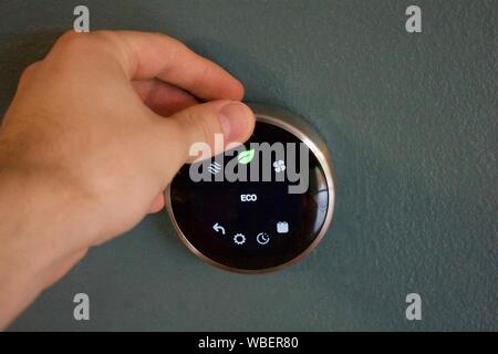 Hand adjusting temperature to save money using smart thermostat Stock Photo