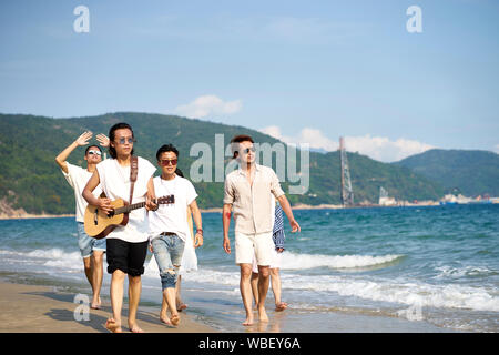 group of young asian adults men walking on beach playing guitar Stock Photo