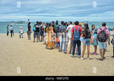 Asian Indian tourists queuing  on Pattaya beach for a boat trip to the distant island of Ko Lan or Koh Larn. Thailand tourism Stock Photo