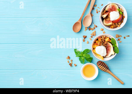 Healthy breakfast or snack figs peach yogurt granola in bowl on blue wooden background. Top view, copy space. Clean eating, dieting, fitness menu conc Stock Photo