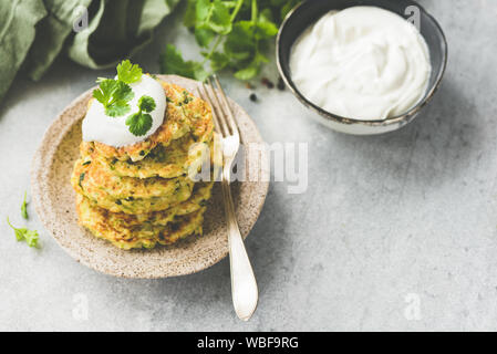 Vegetable fritters of zucchini, cabbage, potato served with sour cream and fresh cilantro. Copy space. Toned image Stock Photo