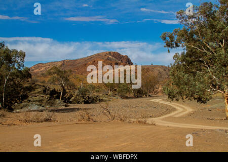 Australian outback landscape at Mount Chambers gorge during drought, with track winding across barren ground among hills under blue sky Stock Photo
