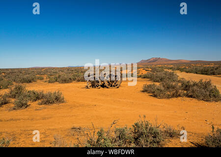 Old horse drawn farm wagon abandoned in remote and arid outback landscape with red soil and low vegetation on plains under blue sky in South Australia Stock Photo