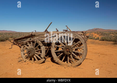Old horse drawn farm wagon abandoned in remote and arid outback landscape with red soil and low vegetation on plains under blue sky in South Australia