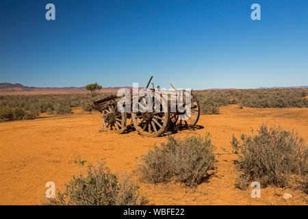 Old horse drawn farm wagon abandoned in remote and arid outback landscape with red soil and low vegetation on plains under blue sky in South Australia Stock Photo