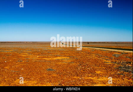 Road stretching across vast red stony barren plains that stretch to distant horizon under blue sky in outback Queensland during drought Stock Photo