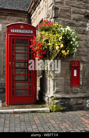 Red telephone box and post box next to a stone building with colourful hanging plants Stock Photo