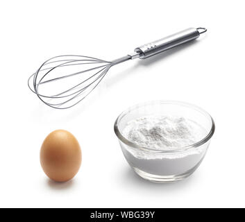 Baking ingredients - balloon whisk, egg and flour isolated on white background Stock Photo