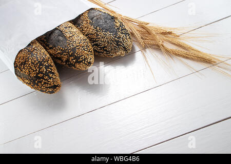Homemade sourdough bread baguettes and wheat in market packet on wooden white background. Food. Stock Photo