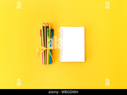Back to school background with opened notepad and variety of colorful pens and pencils tied with yellow silk ribbon on bright yellow backdrop. Copy sp Stock Photo