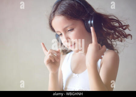 inspired curly little caucasian girl in headphones listening sound of audio music with fingers up Stock Photo