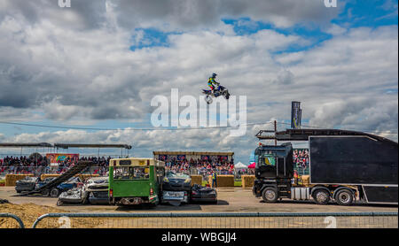A stuntman on a quadbike making a large leap over car stacks and a disused bus during a demonstration at the Monster Truck Nationals held at Santa Pod Stock Photo