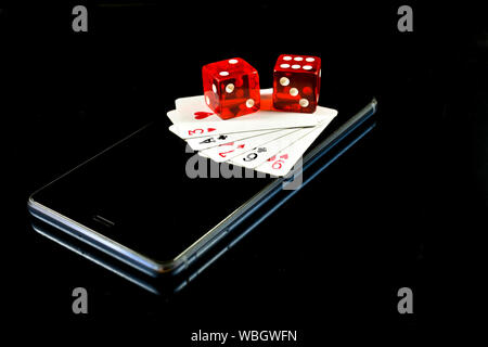 Mobile phone on black background with several playing cards and red dice on display, conceptual image about mobile game industry Stock Photo