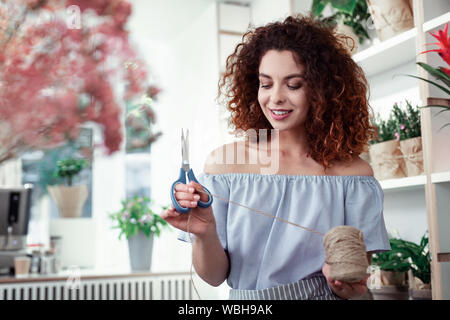 Pretty smiling lady carrying blue scissors and observing thread Stock Photo