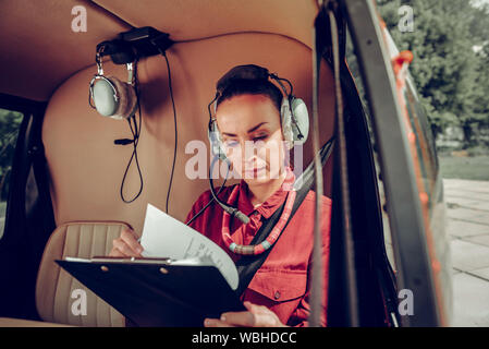 Female pilot wearing red shirt checking the documents in the helicopter Stock Photo