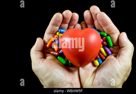 White adult male hands holding together a red human shaped spongy red heart and colored pills , conceptual image about healthcare and medical Stock Photo