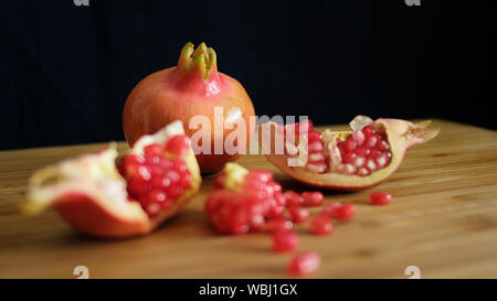 One whole and one open pomegranate or the fruit of Punica granatum revealing clusters of red, juicy seeds, white fibrous arils and thick and waxy peel Stock Photo