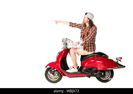 side view of young man sitting on red scooter and pointing with finger isolated on white Stock Photo