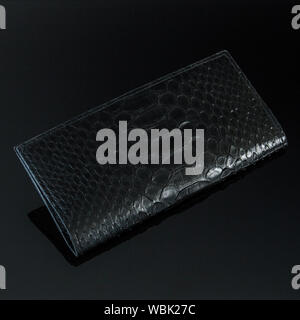 Exotic and luxury set of hand made leather wallet. On a stone tile with background with Plumeria. Python piton snake fashionable handbag, purse, clutc Stock Photo
