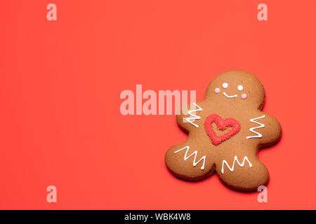 Christmas Gingerbread man sugar cookie in humanoid shape with red heart icing decoration on coral background Stock Photo
