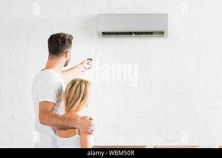 back view of couple with remote control suffering from heat under air conditioner at home Stock Photo