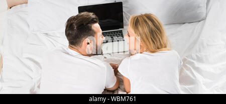 panoramic shot of couple lying in bed and using laptop at home Stock Photo
