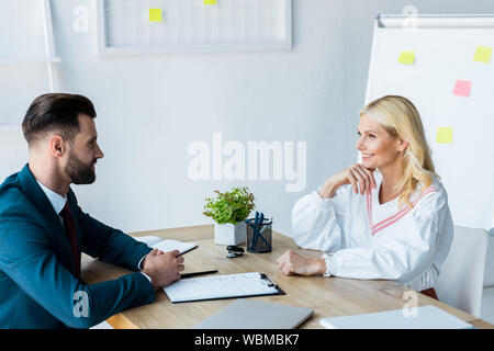 happy blonde woman looking at handsome recruiter with clenched hands Stock Photo