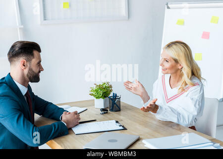 cheerful and bearded recruiter looking at woman gesturing in office Stock Photo