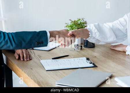 cropped view of recruiter and woman shaking hands near clipboard on table Stock Photo