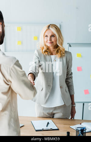 selective focus of blonde recruiter shaking hands with employee in office Stock Photo