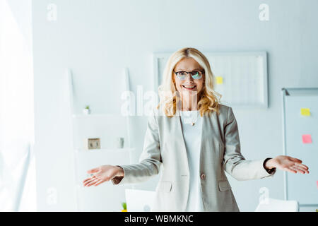 cheerful blonde woman in glasses gesturing in office Stock Photo